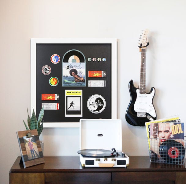 Custom framed music memorabilia hanging on a wall next to a guitar, above a table with a record player and bins of records Hall of Frames Arizona
