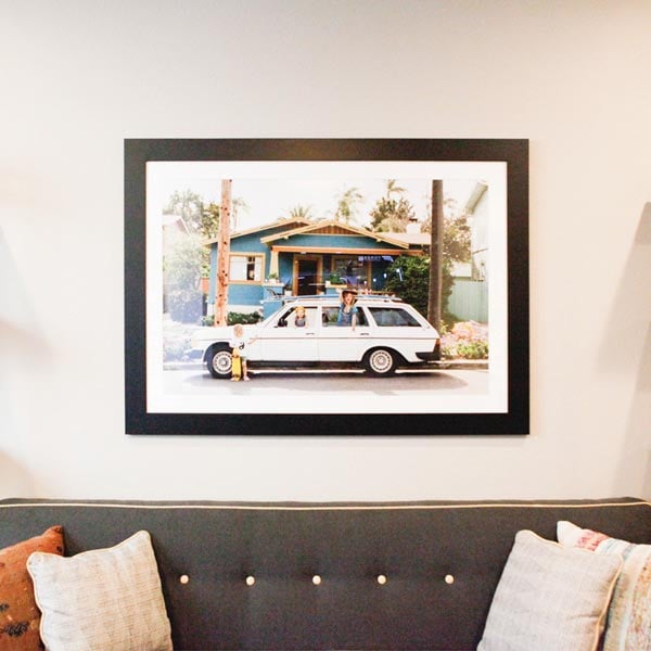 Custom framed photograph of vintage car in front of bungalow, framed in classic black frame and white mat, hanging over couch Hall of Frames Arizona