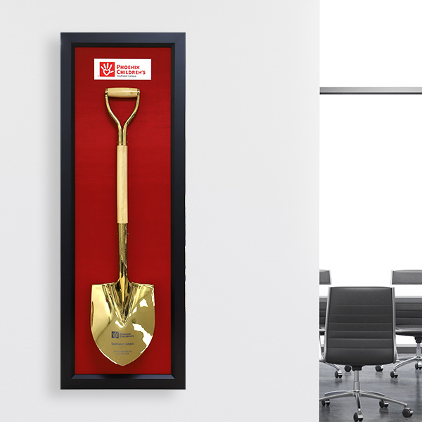 A photo of a framed golden shovel for Phoenix Childrens Hospital displayed in an office setting