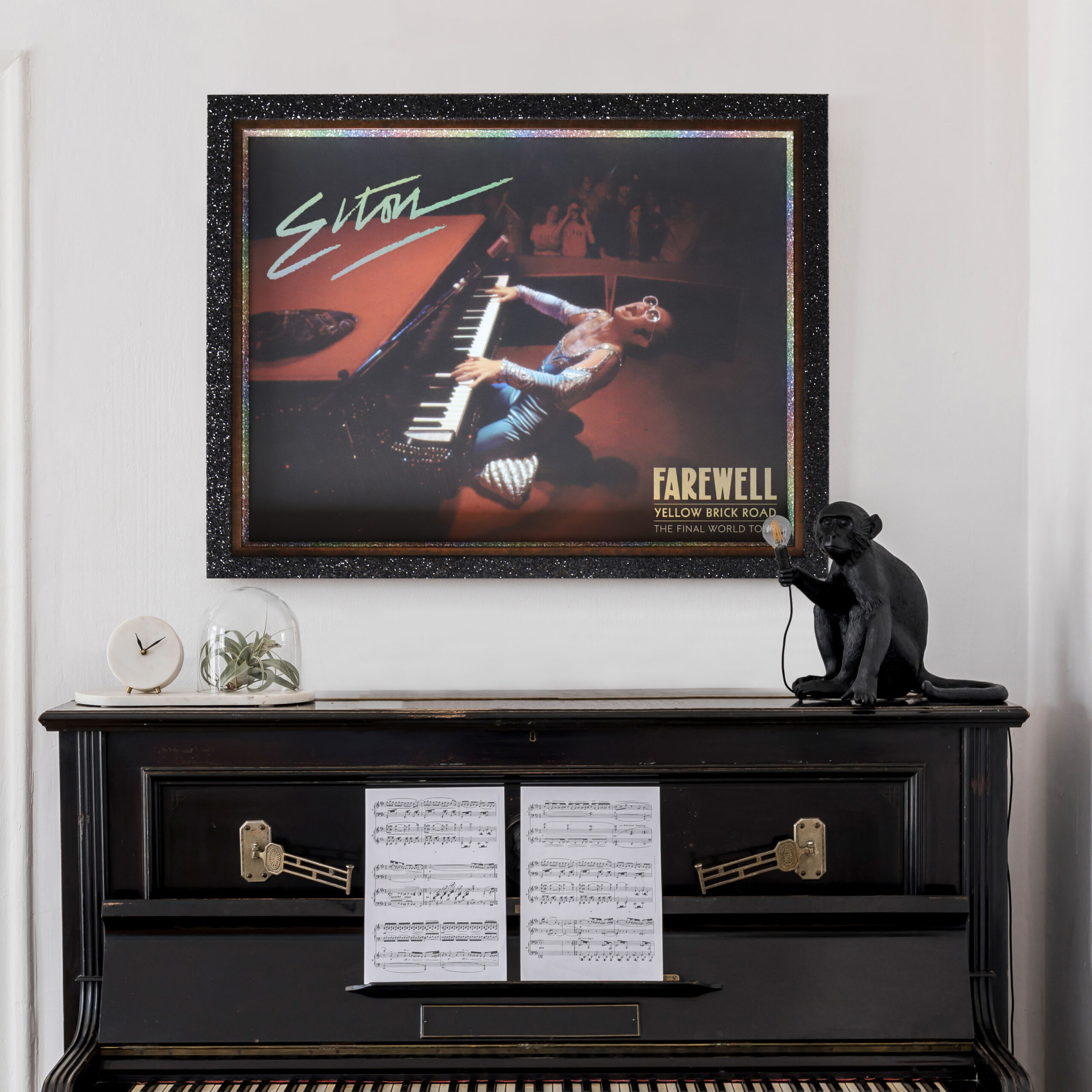 A photo of a framed Elton John Farewell Poster hanging above a piano