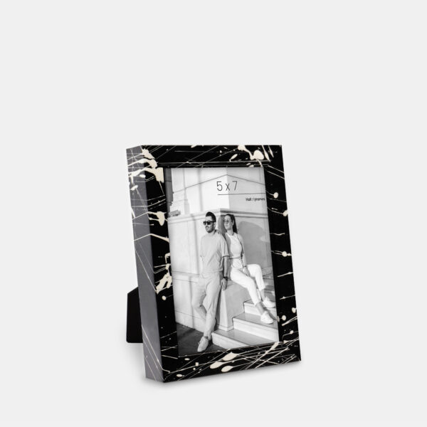 A paint splatter frame in the color Night Hush featuring a modern, architectural photo of a couple. 