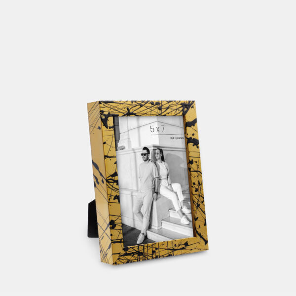 A paint splatter frame in the color Oro Drip featuring a modern, architectural photo of a couple. 