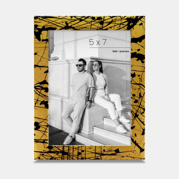 A paint splatter frame in the color Oro Drip featuring a modern, architectural photo of a couple. 