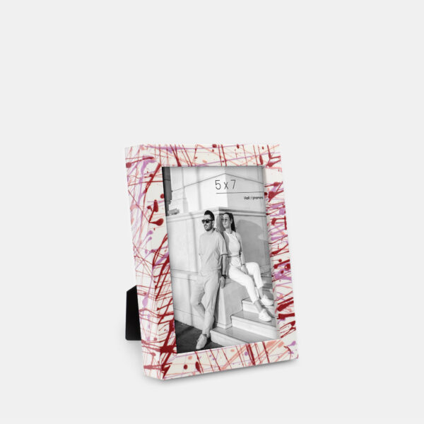 A paint splatter frame in the color Rebel Rose featuring a modern, architectural photo of a couple. 