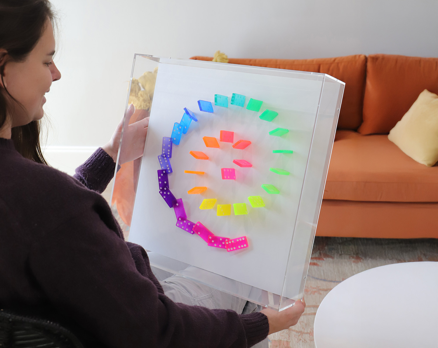 A photo of an set of colorful dominoes set up to appear they are falling, preserved in an clear acrylic box.
