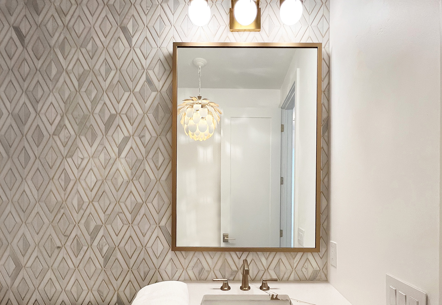 A photo of a mirror with a thin metal gold frame in a bathroom.