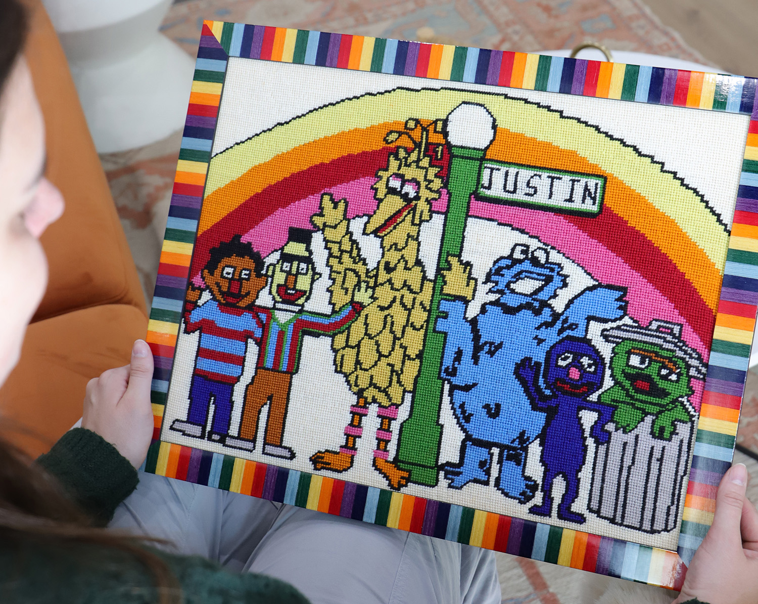 A photo of a vintage Sesame Street needlepoint framed in a colorful rainbow frame.