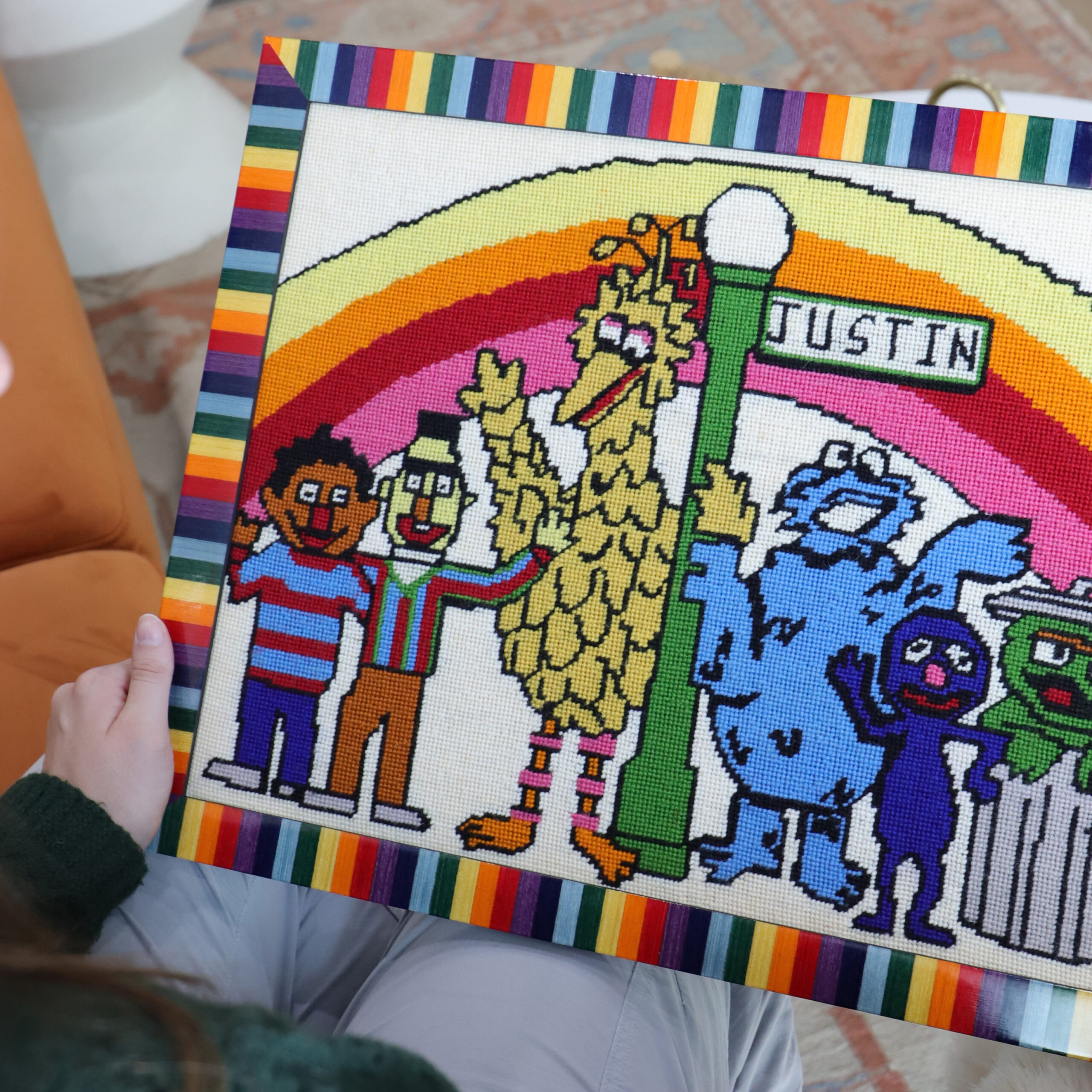 A photo of a vintage Sesame Street needlepoint framed in a colorful rainbow frame.