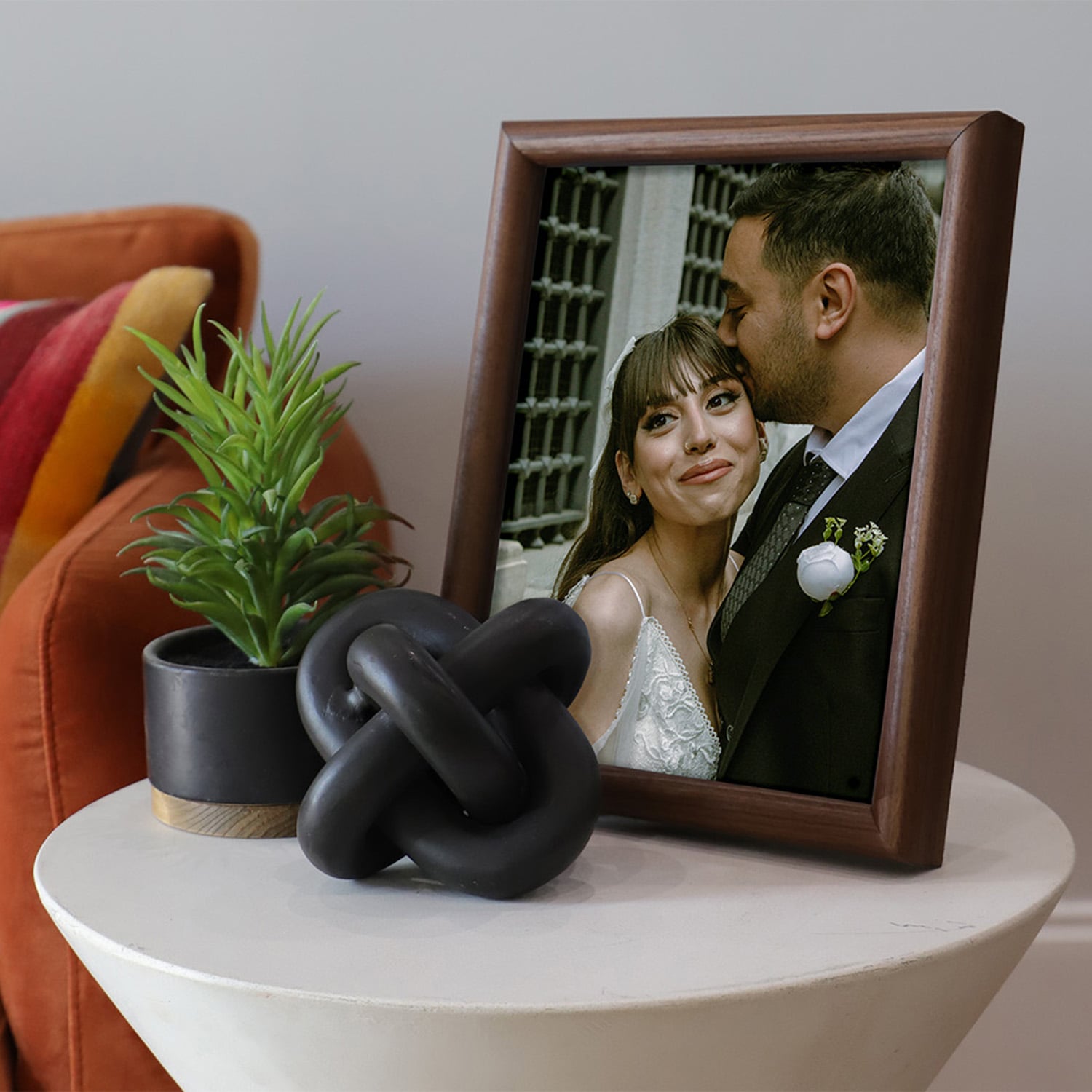 A photo of a wooden tabletop featuring a image of a married couple sitting on a side table next to a couch.