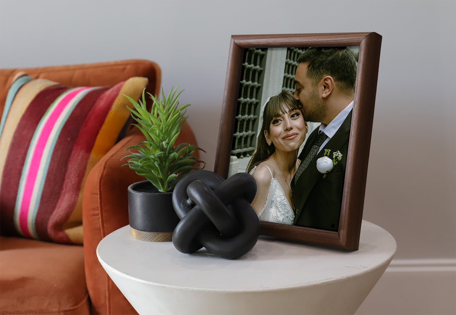 A photo of a wooden tabletop featuring a image of a married couple sitting on a side table next to a couch.