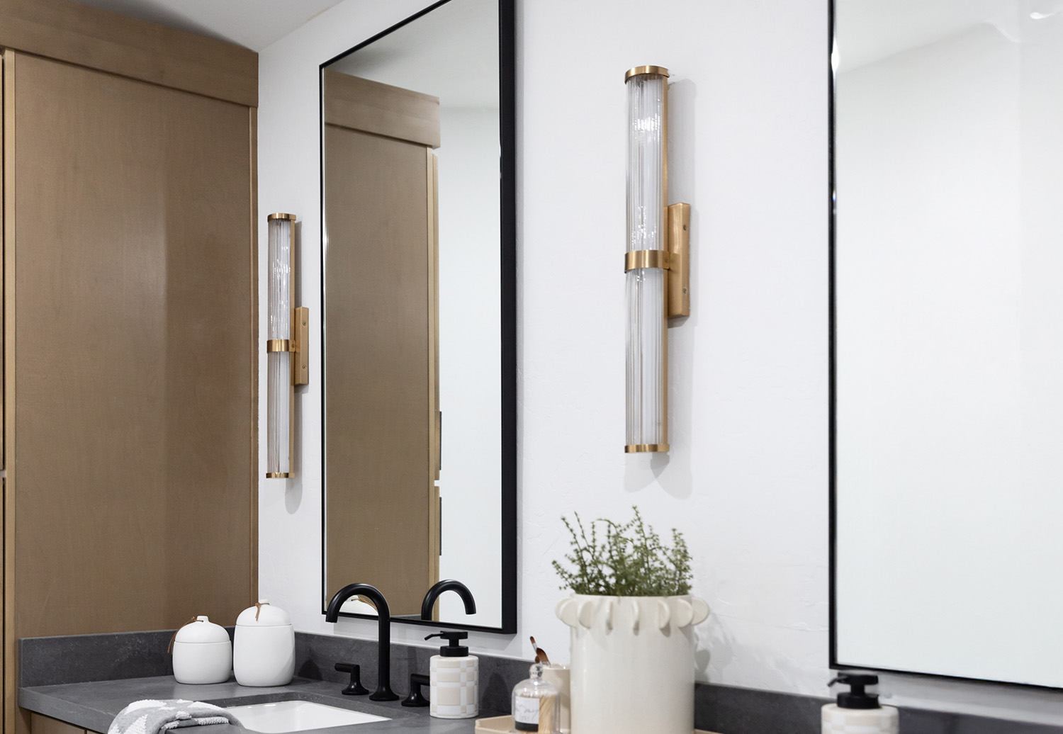 Custom framed bathroom mirror with black frame, brass sconces, and modern vanity in a minimalist bathroom design.