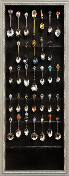 Decorative silver-finished shadowbox frame displaying a collection of vintage souvenir travel spoons.