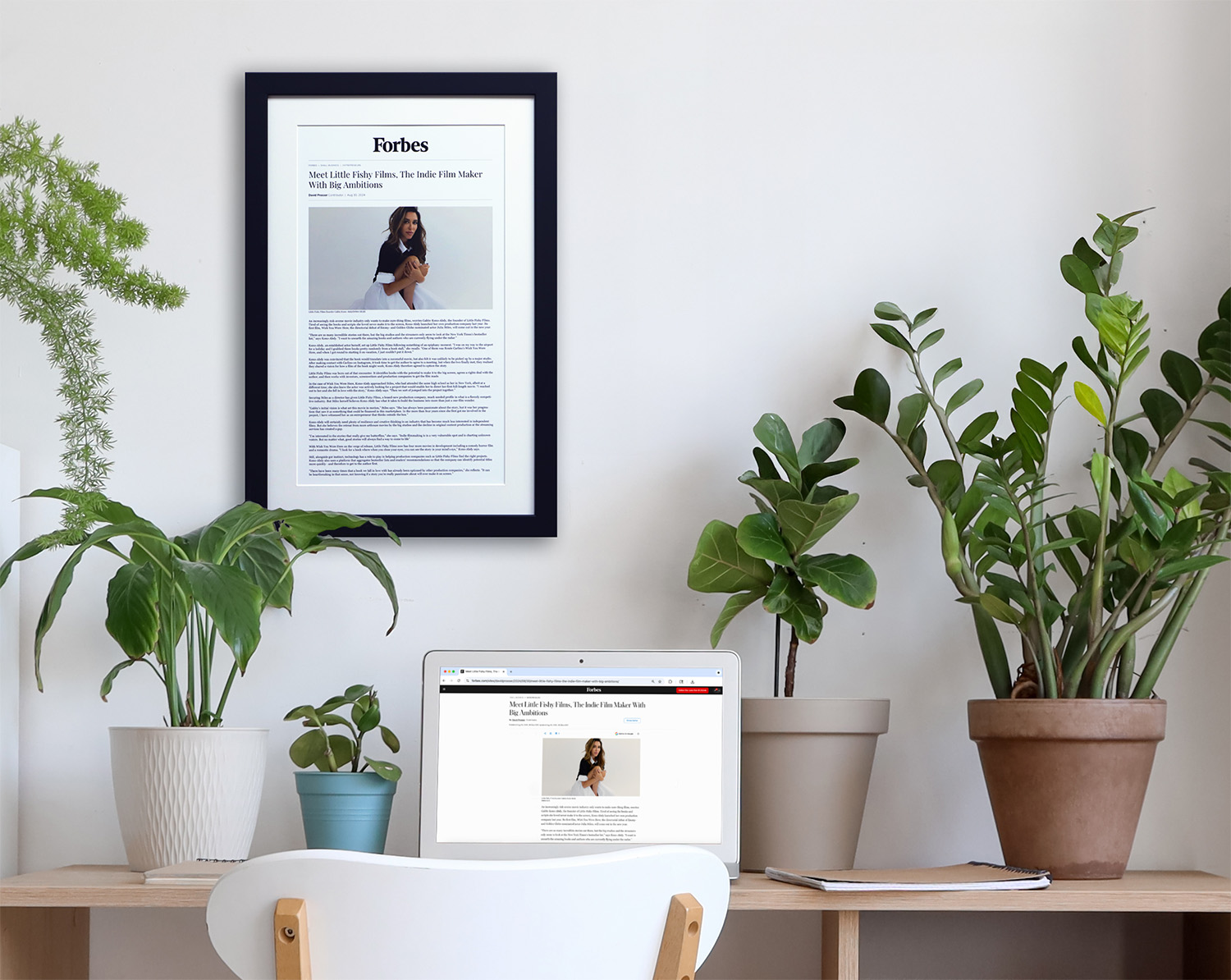 Custom framed online article wall decor above a modern desk with laptop and indoor plants, styled home office inspiration.