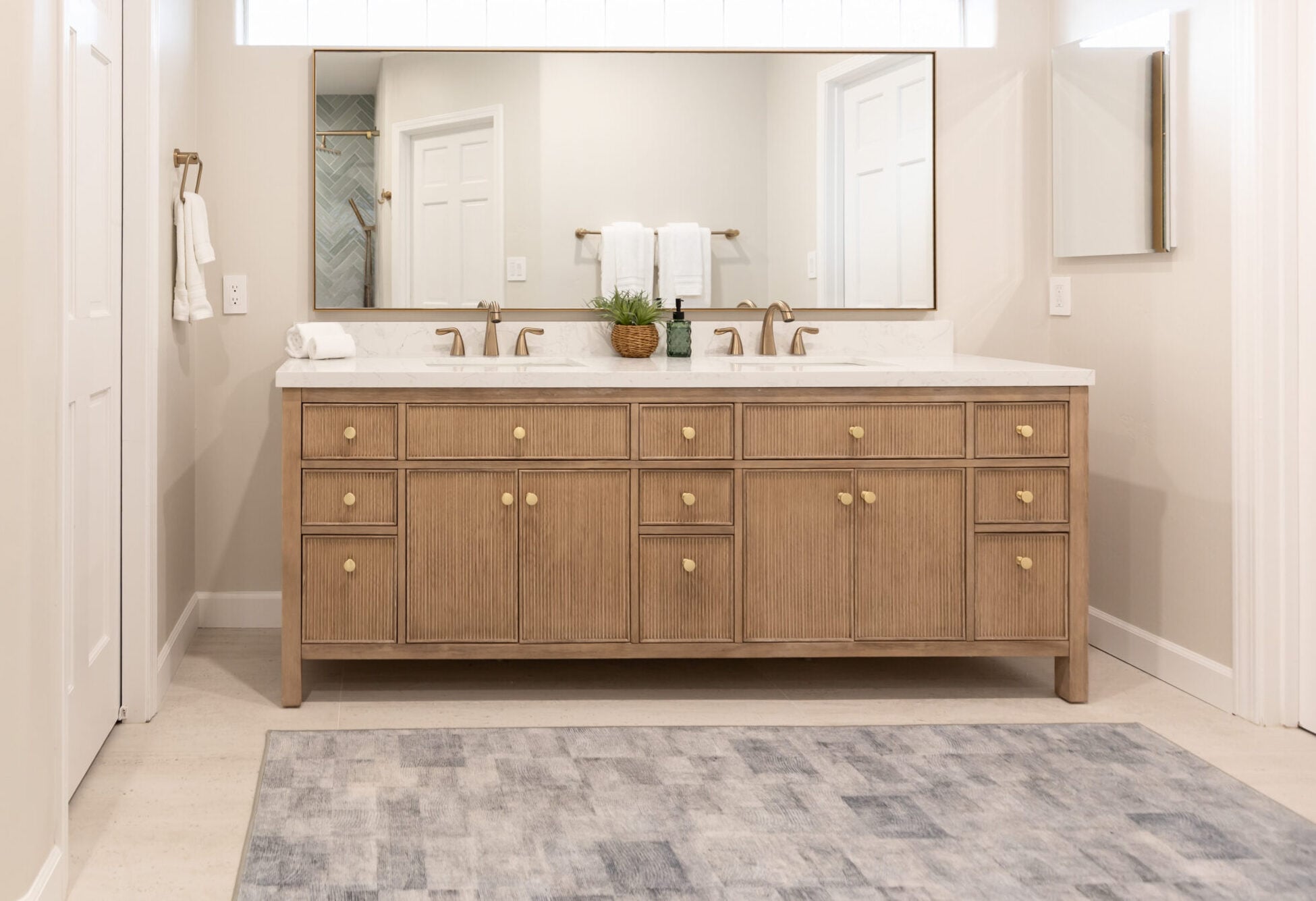 Large horizontal wall mirror with a thin brass metal frame installed over a double-sink bathroom vanity with warm wood cabinets.