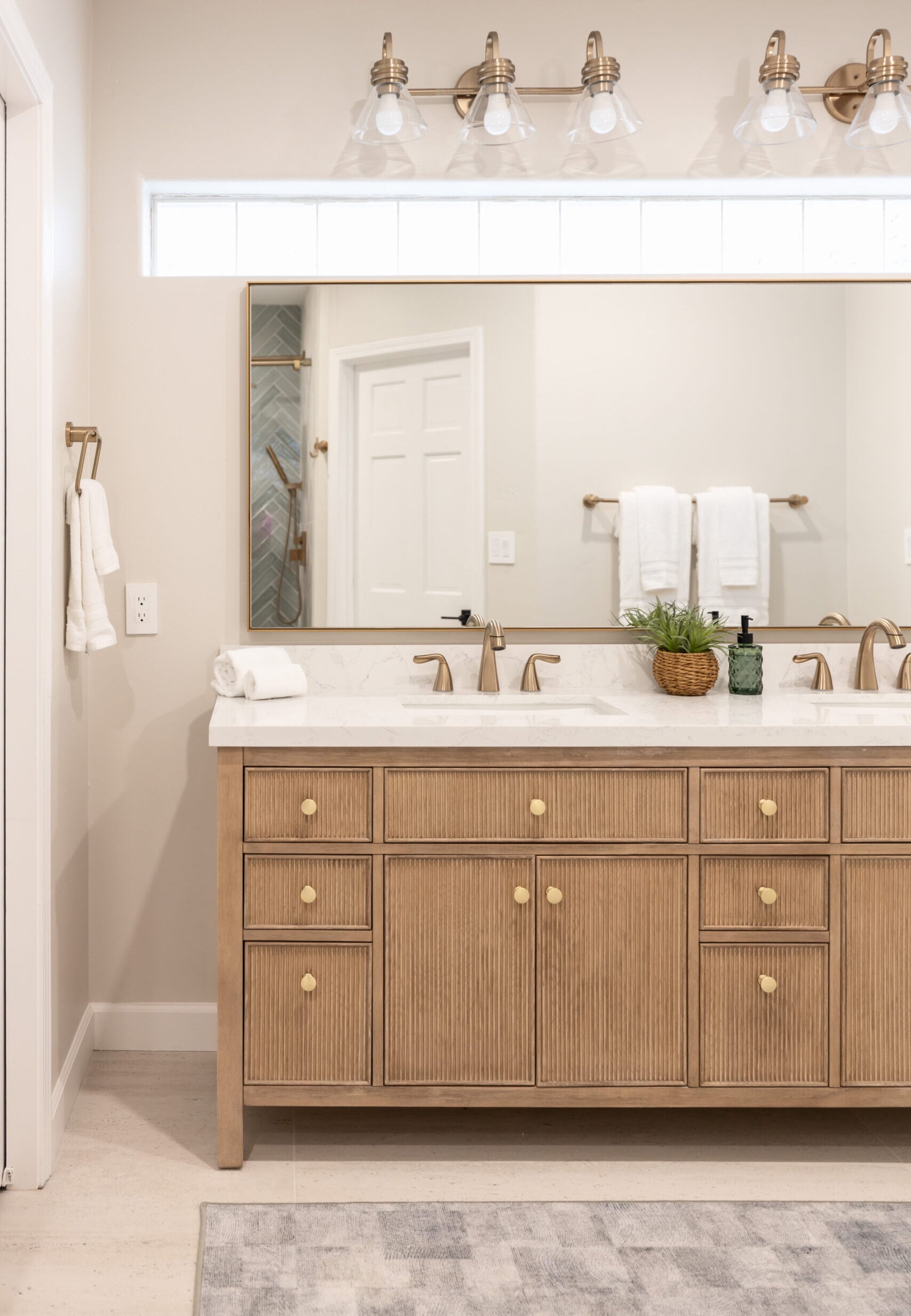 Large horizontal wall mirror with a thin brass metal frame installed over a double-sink bathroom vanity with warm wood cabinets.