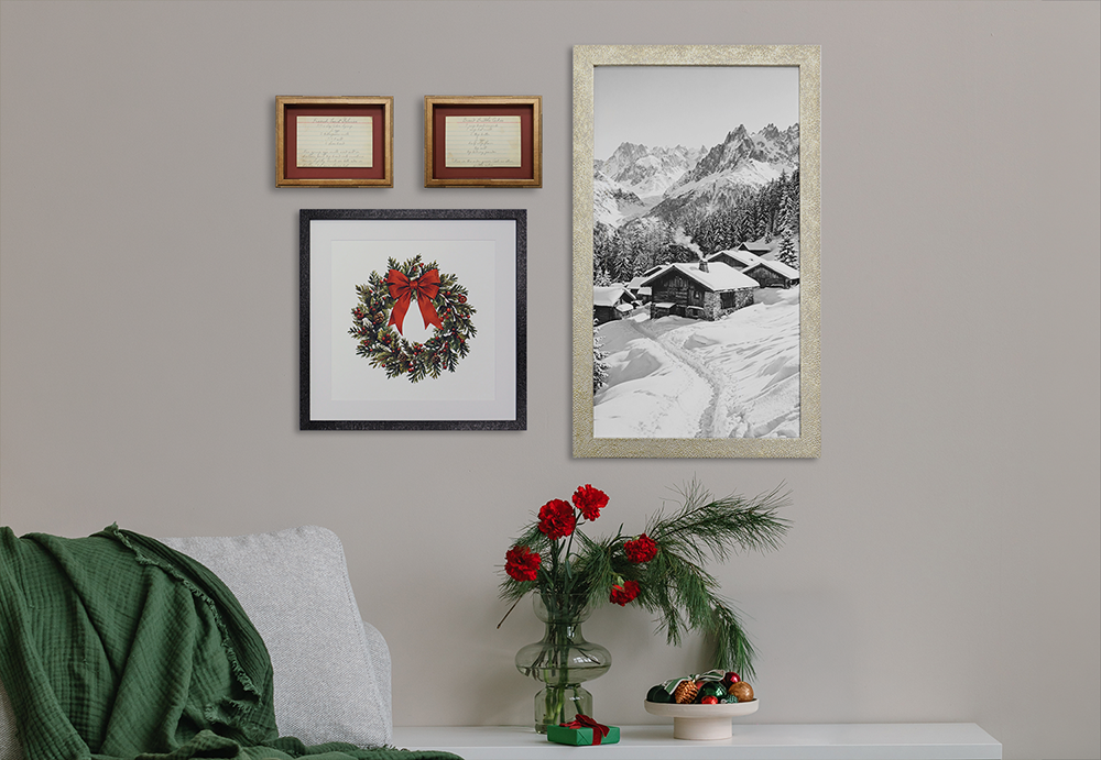Curated holiday gallery wall above a sofa featuring framed winter cabin photography, a Christmas wreath print, and vintage handwritten notes in coordinating frames.